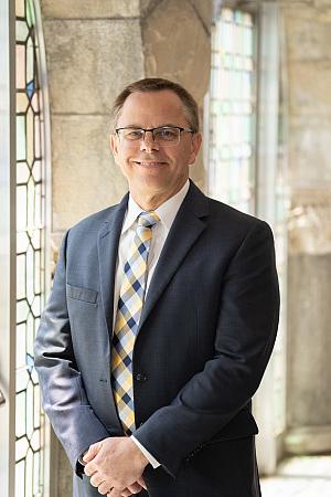 President Eric Boynton stands next to the stained glass doorways in Eaton Chapel.